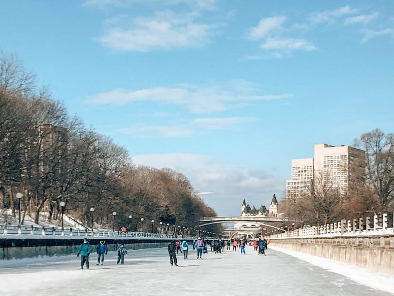 People skating on the Rideau Canal in winter skating towards the Chateau Laurier on a clear sunny day.