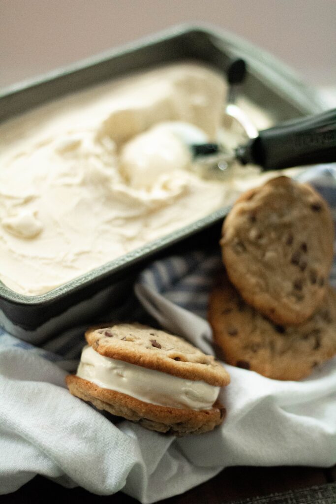 A tub of ice cream with ice cream an ice cream cookie sandwich.