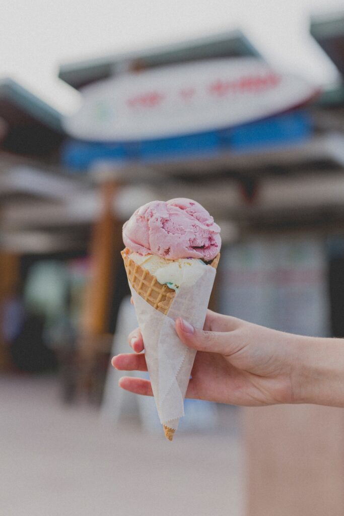 A person's hand holding strawberry flavored ice cream in a waffle cone.